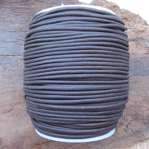 Può includere: Un rotolo di cordoncino in pelle marrone scuro. Il cordoncino è avvolto strettamente attorno a un rotolo di cartone bianco.