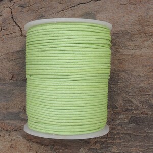 Può includere: Un rocchetto di cordoncino di cotone cerato verde chiaro. Il cordoncino è avvolto strettamente attorno a un rocchetto di plastica bianca.