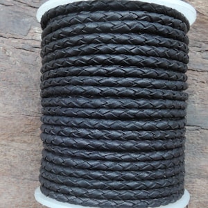 Puede incluir: Un carrete de cordón de cuero trenzado negro. El cordón está enrollado apretado y tiene un acabado liso y pulido.