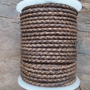 Può includere: Un rotolo di cordoncino in pelle marrone, intrecciato a forma di diamante. Il cordoncino è avvolto strettamente attorno al rotolo, creando un aspetto spesso e testurizzato.