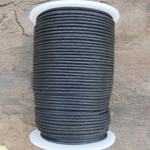 Peut inclure: Une bobine de cordon en coton ciré noir. Le cordon est enroulé serré autour d'une bobine en plastique blanc. L'arrière-plan est une surface en bois vieilli. Ce cordon est adapté à la création de bijoux et à l'artisanat.