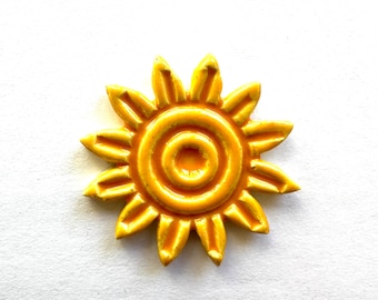 Può includere: Un sole in ceramica giallo con un design a cerchi concentrici. Il sole ha 12 punti.
