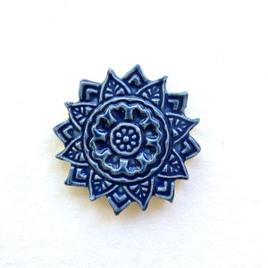 Peut inclure: Un carreau de mandala en céramique bleu avec un motif floral détaillé. Le carreau a une surface texturée en relief et un glaçage bleu clair.