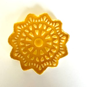 Puede incluir: Un plato de cerámica amarillo con un diseño de estrella. El plato tiene un patrón intrincado y elevado de triángulos y círculos.