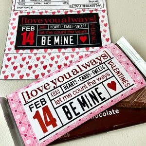 May include: A pink and white Valentine's Day chocolate bar wrapper with the text "[love you always]" and "FEB 14 BE MINE". The wrapper is decorated with red hearts and white polka dots. The chocolate bar is visible behind the wrapper.