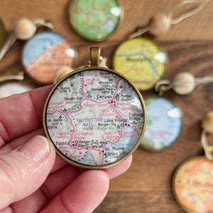 May include: A round pendant with a map of Yellowstone National Park, featuring a brass-colored bezel and a clear, domed surface. The map shows roads, landmarks, and text. Other map pendants are visible in the background.
