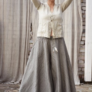 May include: A woman wearing a light beige linen top with a long tie and a pair of wide-legged, striped linen pants.