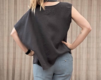 May include: A dark gray sleeveless top with a draped design and a matching scarf detail. The top is paired with light blue pants. The model has blonde hair pulled back in a ponytail.