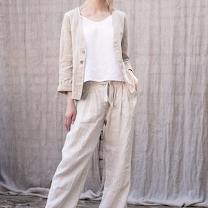 May include: A woman wearing a light beige linen blazer and matching wide-leg pants. The blazer has a single button closure and the pants have a drawstring waist.