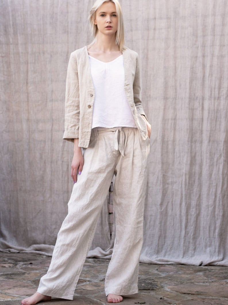 May include: A woman wearing a light beige linen blazer and matching wide-leg pants. The blazer has a single button closure and the pants have a drawstring waist.