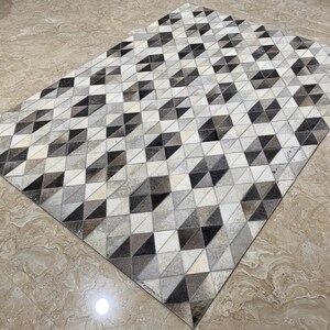 May include: Rectangular rug featuring a geometric pattern of triangles in black, grey, and cream. The rug's design creates a repeating pattern. It appears to be made from a natural material.