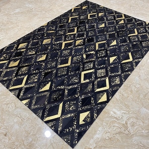 May include: A rectangular rug with a geometric pattern. The rug features a repeating design of black and gold diamond shapes. The gold sections have a speckled appearance, adding texture. The rug is likely made of a durable material.
