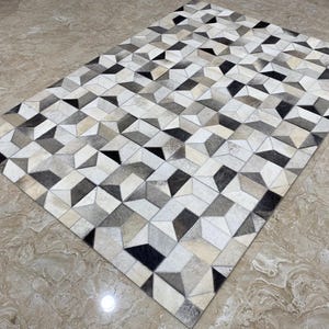 May include: Geometric patterned rug in shades of gray, black, and cream. The rug features a repeating 3D cube design. The rug is rectangular and appears to be made of a soft material.