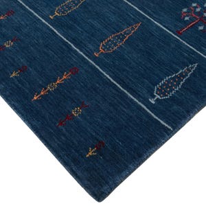 Angled close view of corner, thin low pile fold highlights soft wool weave on modern boho navy rug