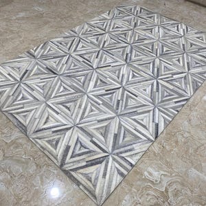 Op de afbeelding: Een rechthoekig tapijt met een geometrisch patroon. Het tapijt heeft een herhalend ontwerp van driehoeken en sterren in tinten grijs, wit en zwart. Het tapijt is gemaakt van een zacht materiaal en is geschikt voor een woon- of slaapkamer.