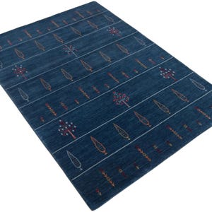 Angled perspective shows low pile texture on handwoven gabbeh carpet, deep navy stripes and motifs