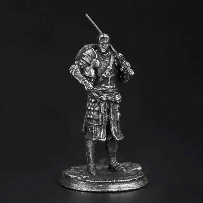 K&ouml;nnte beinhalten: Eine silberfarbene Miniaturfigur aus Metall, die einen Krieger auf einem runden Sockel darstellt. Die Figur tr&auml;gt eine detaillierte Plattenr&uuml;stung, h&auml;lt ein Schwert auf der Schulter und einen Helm unter dem Arm, mit feinen Texturen.