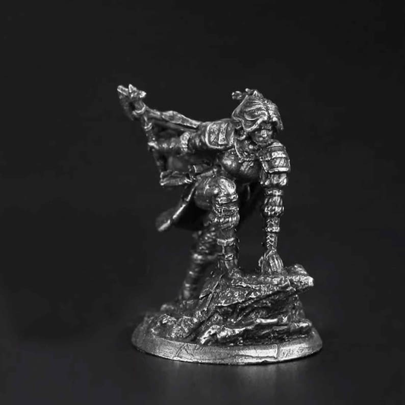 K&ouml;nnte beinhalten: Eine silberfarbene Metallminiaturfigur eines Kriegers in Plattenr&uuml;stung, in dynamischer Pose mit einem Fu&szlig; auf einem felsigen Sockel. Die Figur h&auml;lt eine Stangenwaffe und tr&auml;gt einen wehenden Umhang, dargestellt in detailliertem Metallrelief.