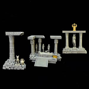 May include: Three-piece miniature Egyptian temple set in gray stone. The set includes columns, statues, a sarcophagus, and a golden Anubis figure. The structures are arranged on a black background.