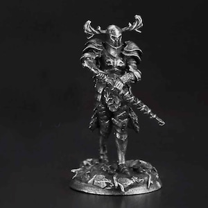 K&ouml;nnte beinhalten: Eine silberfarbene Metallminiaturfigur eines Kriegers in Plattenr&uuml;stung und einem Helm mit gro&szlig;en, verzweigten Geweihen. Die Figur steht auf einem strukturierten, felsigen Sockel und h&auml;lt ein langes, schmales Schwert, das nach unten zeigt.
