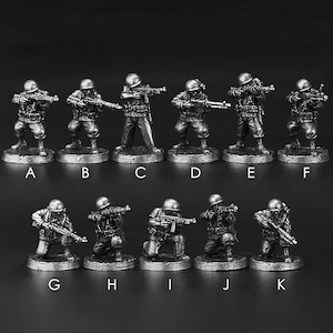 May include: Set of 11 miniature metal soldiers in various poses, some standing and some kneeling, holding rifles. The soldiers are painted in a silver colour and are arranged in two rows on a black background.
