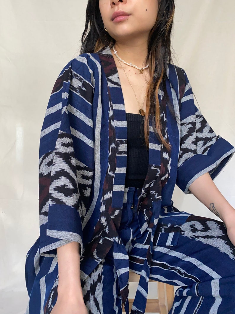K&ouml;nnte beinhalten: Ein zweiteiliges Set aus Kimono und Hose mit blau-wei&szlig;em Muster. Die Jacke hat ein Streifendesign mit dunkelblauem Grund und wei&szlig;en Streifen. Die Hose hat ein &auml;hnliches Muster. Das Outfit ist aus einem weichen, flie&szlig;enden Stoff gefertigt.