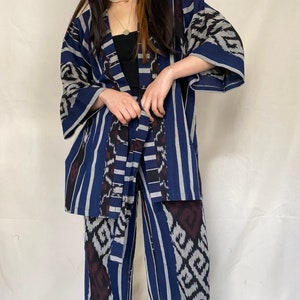 K&ouml;nnte beinhalten: Ein zweiteiliges Set mit einem blau, wei&szlig; und dunkelrot gemusterten Design. Das Set besteht aus einer Kimono-Jacke mit weiten &Auml;rmeln und einer passenden Hose mit weitem Bein. Der Stoff hat ein Streifen- und geometrisches Muster.