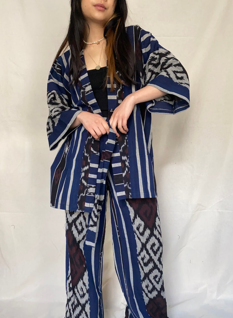 K&ouml;nnte beinhalten: Ein zweiteiliges Set mit einem blau, wei&szlig; und dunkelrot gemusterten Design. Das Set besteht aus einer Kimono-Jacke mit weiten &Auml;rmeln und einer passenden Hose mit weitem Bein. Der Stoff hat ein Streifen- und geometrisches Muster.