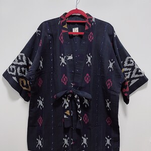 May include: A dark blue kimono-style jacket with a patterned design. The jacket features a V-neck, short sleeves, and a tie closure. The pattern includes white, pink, and yellow accents. The jacket is hanging on a red hanger.