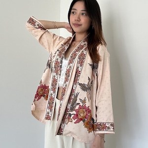 Op de afbeelding: Een lichtroze kimono met een bloemen- en vogelprint. De kimono heeft lange mouwen en een brede kraag. De stof is zacht en soepel.