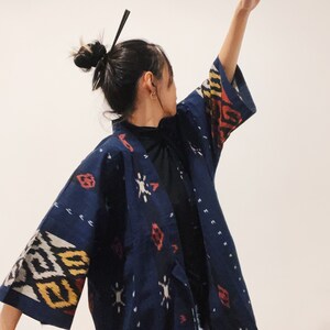 May include: A dark blue kimono-style jacket with a geometric pattern in white, yellow, and red. The jacket has wide sleeves and a wrap-around design. The fabric appears to be a woven material.