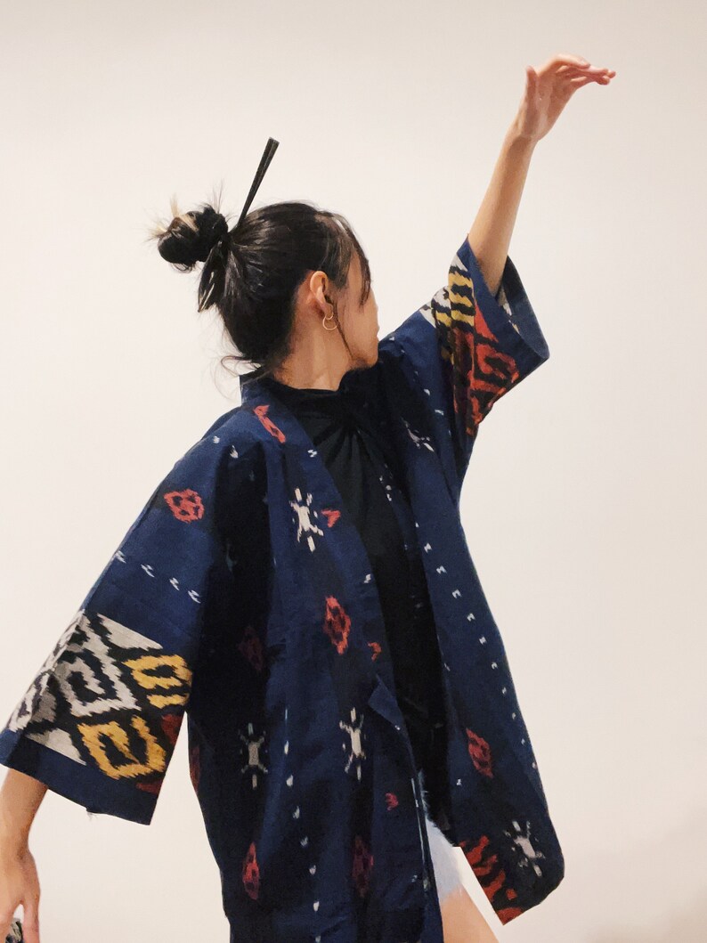 May include: A dark blue kimono-style jacket with a geometric pattern in white, yellow, and red. The jacket has wide sleeves and a wrap-around design. The fabric appears to be a woven material.