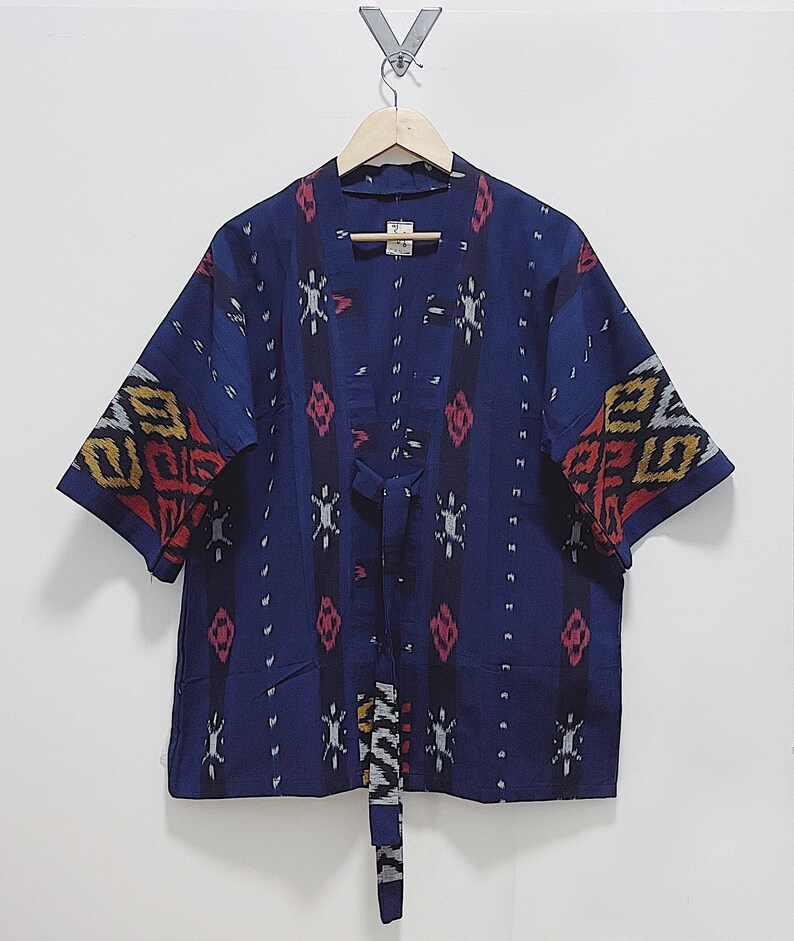 May include: A navy blue kimono-style jacket with short sleeves, featuring a patterned design in red, yellow, and white. The jacket has a tie closure and is hanging on a wooden hanger against a white background. The sleeves have a decorative pattern.