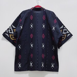 May include: A dark blue kimono-style jacket with a patterned design. The pattern includes white, red, and yellow accents. The jacket is hanging on a red hanger against a white wall.