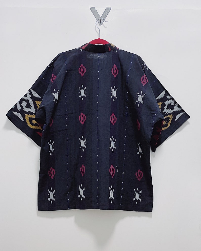 May include: A dark blue kimono-style jacket with a patterned design. The pattern includes white, red, and yellow accents. The jacket is hanging on a red hanger against a white wall.