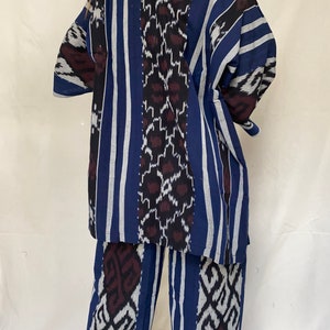 K&ouml;nnte beinhalten: Ein zweiteiliges Set mit blauem, wei&szlig;em und schwarzem Muster. Das Oberteil ist eine kurz&auml;rmlige Jacke im Kimono-Stil. Die Hose ist weit geschnitten. Der Stoff hat vertikale Streifen und geometrische Muster.