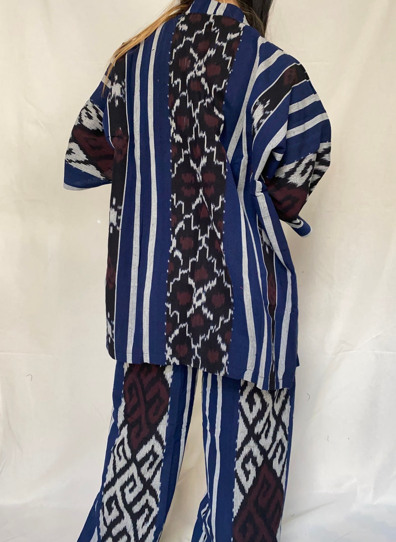 K&ouml;nnte beinhalten: Ein zweiteiliges Set mit blauem, wei&szlig;em und schwarzem Muster. Das Oberteil ist eine kurz&auml;rmlige Jacke im Kimono-Stil. Die Hose ist weit geschnitten. Der Stoff hat vertikale Streifen und geometrische Muster.