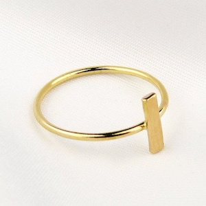 May include: A gold ring with a thin band and a vertical bar accent.