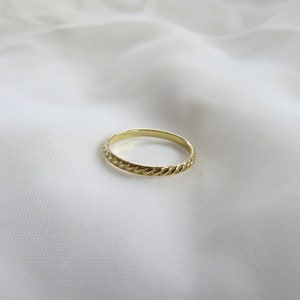 May include: A simple gold band ring with a rope-like design.