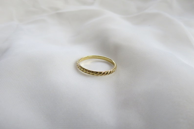May include: A simple gold band ring with a rope-like design.