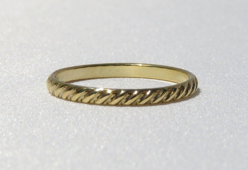 May include: A simple gold band ring with a twisted rope design.