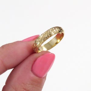 May include: A gold band ring with a delicate floral design engraved around the entire band.