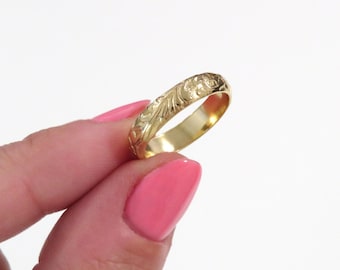 May include: A gold band ring with a delicate floral design engraved around the entire band.
