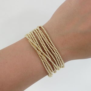 May include: A set of gold beaded bracelets stacked on a wrist. The bracelets are made of small, round beads that are evenly spaced.