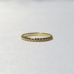 May include: A simple gold band ring with a twisted design.