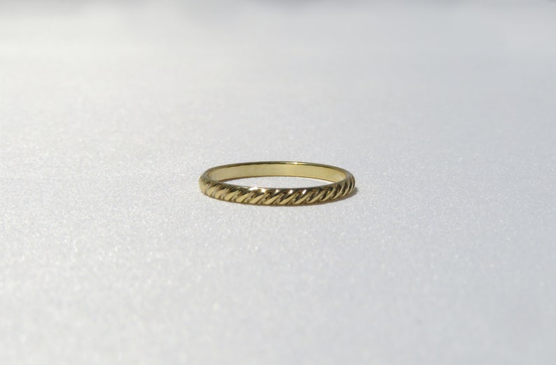 May include: A simple gold band ring with a twisted design.
