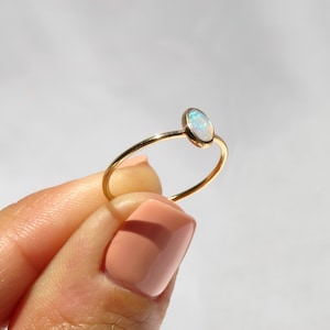 May include: A delicate gold ring with a small oval opal gemstone. The opal has a milky white color with hints of blue and green.