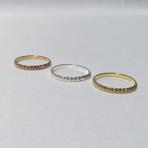 May include: Three simple, thin, braided rings in gold, silver, and rose gold.