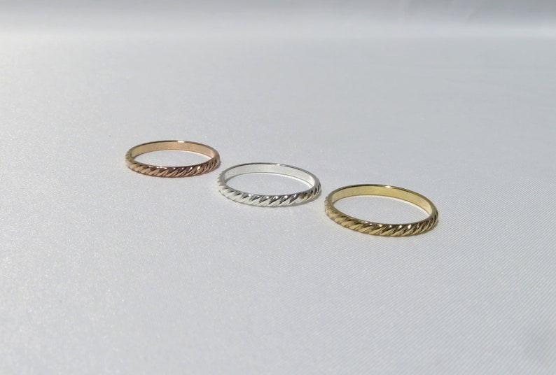 May include: Three simple, thin, braided rings in gold, silver, and rose gold.