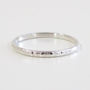 May include: A thin silver band with a textured design. The band is smooth and shiny.